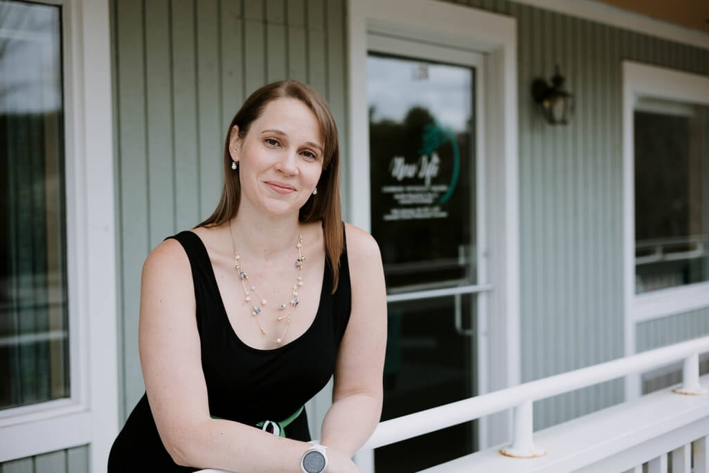 Dr. Jen Blanchette leaning on the railing outsider her office wearing a black tank top