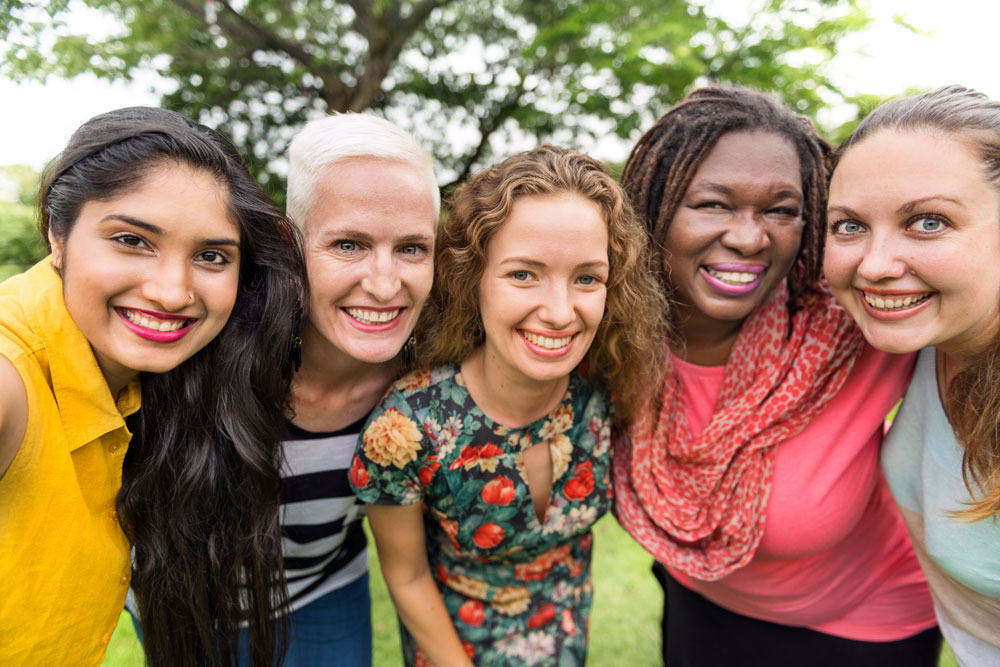 A group of diverse women close together smiling at the camera.